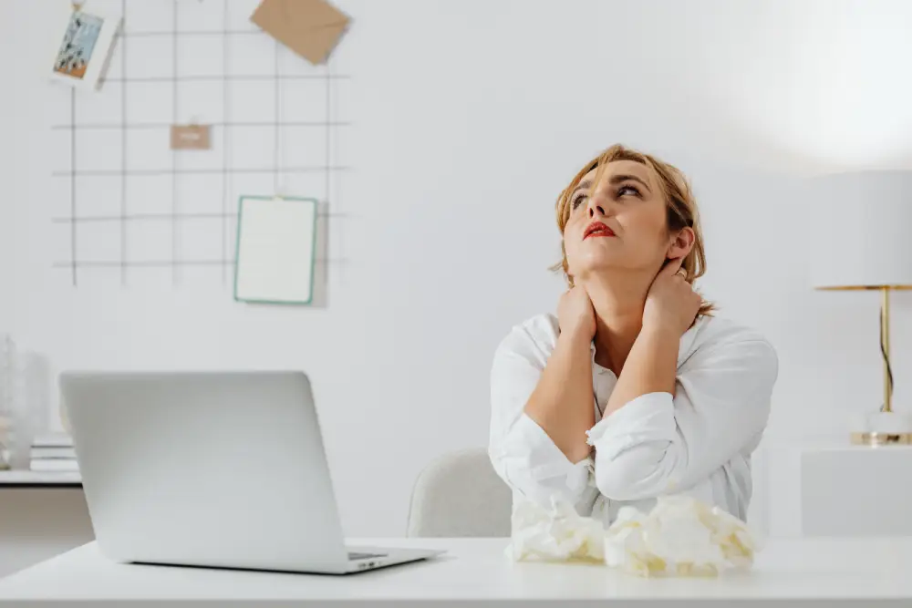 Person experiencing neck pain while working at a desk.
